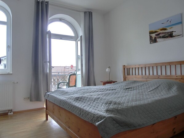 A bedroom with a wooden bed, a view through a window, and a painting on the wall.