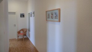 A hallway with a wooden floor, a door at the end, and a chair with a cushion. - Vacation apartment LVC4 - 2-room apartment for 4 pers. with WLAN (Graal-Müritz)
