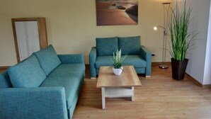 A living room with two teal sofas, a wooden coffee table, a potted plant, a floor lamp, and a painting of a beach scene on the wall.