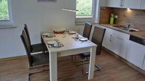 A modern kitchen with white cabinets, a wooden countertop, and a dining area with a white table and chairs.