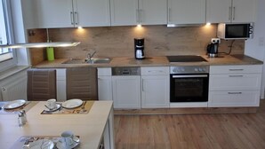 A modern kitchen with white cabinets, a wooden countertop, a built-in microwave, a coffee maker, and a dishwasher.
