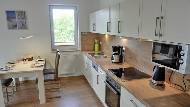 A modern kitchen with white cabinets, a wooden countertop, a built-in oven, a microwave, and a coffee maker.
