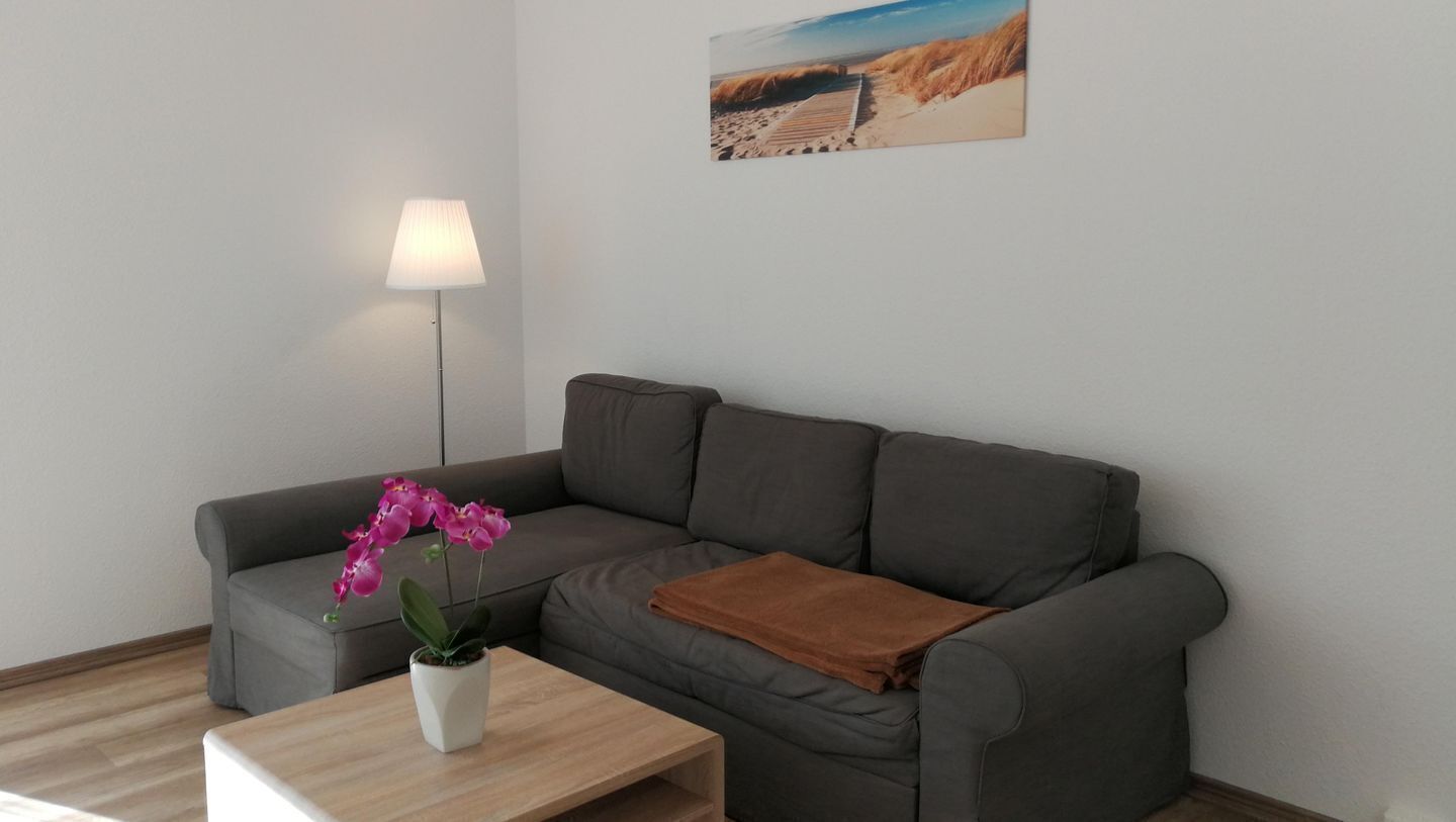 Ein modernes Wohnzimmer mit einem grauen Sofa, einem Holztisch, einer pinkfarbenen Orchidee, einer braunen Decke und einer Stehlampe.