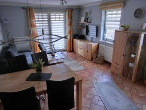 Ein modernes Wohnzimmer mit Essbereich, ausgestattet mit einer Couch, einem Holztisch und einem an der Wand befestigten Fernseher.