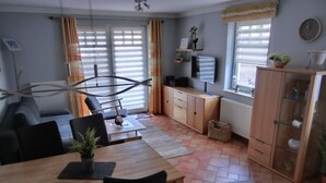 A modern living room with a dining area, featuring a sofa, a wooden dining table, and a TV mounted on the wall.