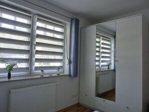 Un dormitorio con un armario grande, una ventana con persianas, un radiador y un espejo.