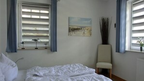 A bedroom with a bed, a chair, a window with blinds, and a painting on the wall.