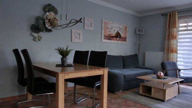 A modern living room with a dining table, chairs, a sofa, and a small coffee table. - Vacation Rental K36 - Central 2-Bedroom Apartment for 3 People, Terrace (Graal-Müritz)