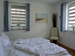 Ein Schlafzimmer mit einem Bett, einem Sessel, einem Fenster mit Jalousien und einem Bild an der Wand.