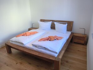 Een tweepersoonsbed met houten hoofdbord en voetenbord, twee nachtkastjes en een houten vloer.