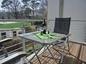 Een balkon met een tafel, stoelen en een fles wijn.