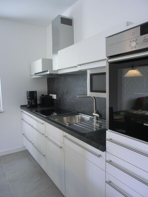 A modern kitchen with a stainless steel sink, a built-in oven, and white cabinetry.