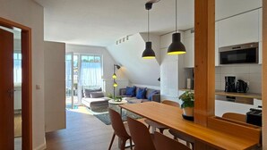 A modern kitchen with a dining area, wooden flooring, and a view of the living room.