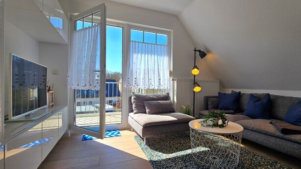 A modern living room with a sofa, a coffee table, and a TV. There is a sliding glass door leading to an outdoor area.