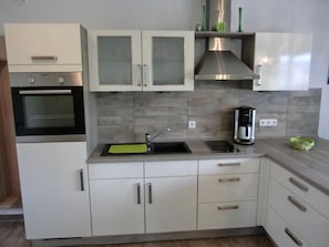 A modern kitchen with white cabinets, a stainless steel range hood, a built-in oven, a sink with a green mat, and a coffee maker.