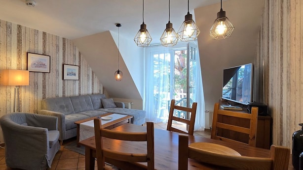 A living room with a sofa, a dining table with chairs, a TV, and a lamp. - Apartment K21 "Storchennest" - 3-room apartment for 6 pers. on the 2nd floor with balcony (Graal-Müritz)