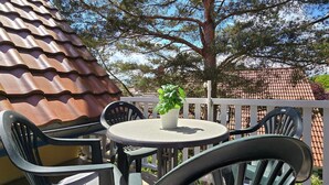 An outdoor patio with a round table and chairs, a potted plant, and a view of a red-tiled roof and trees. - Apartment K21 "Storchennest" - 3-room apartment for 6 pers. on the 2nd floor with balcony (Graal-Müritz)