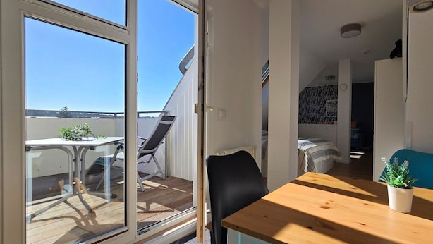 Una stanza piccola e open space con un tavolo di legno, una sedia nera e una sedia blu. C'è una porta scorrevole in vetro che dà su un'area esterna con tavolo e sedie.