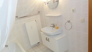 Un baño con bañera, lavamanos con espejo, toallero y retrete.