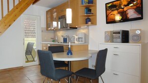 Una cocina compacta con comedor, armarios de madera, televisor integrado y cafetera.