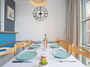 A dining room with a white table set for four, a wall clock, and a window with curtains.