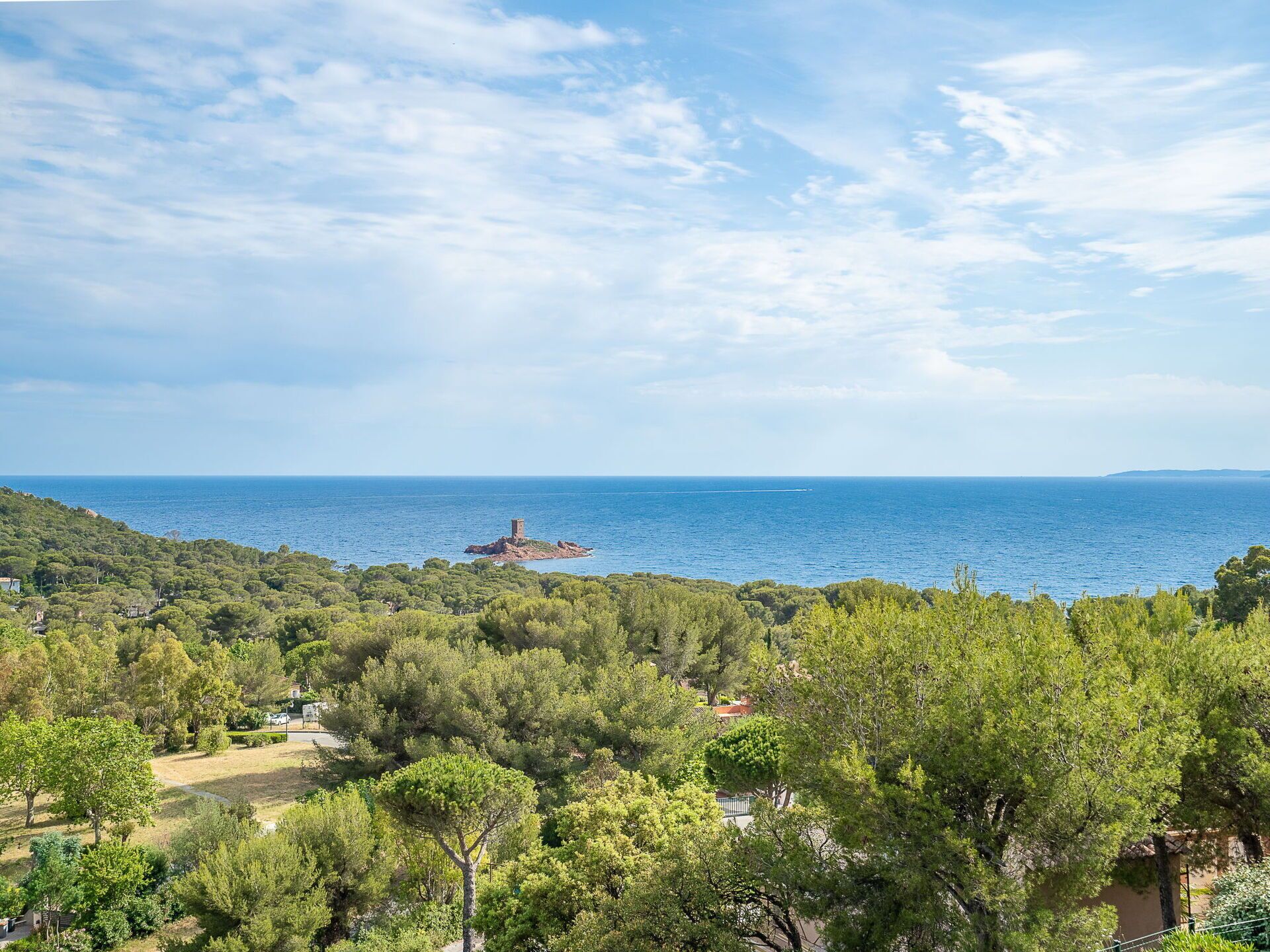 Un paysage côtier avec une tour sur une petite île, entourée d’une végétation luxuriante et sous un ciel dégagé.