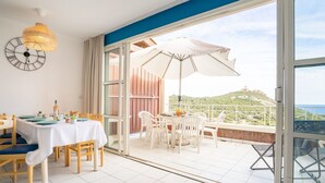 Un comedor con una mesa preparada para dos personas, un reloj en la pared y vistas a un paisaje montañoso a través de amplios ventanales.