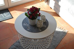 Ein runder, weißer Tisch mit einer grauen Filzauflage, einem Blumentopf und zwei Kerzenständern auf einem Fliesenboden.