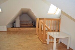 Ein kleines Schlafzimmer im Dachgeschoss mit einem Holzstockbett, einem weißen Tisch und einem Holckrippenbett.