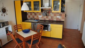A compact kitchen with yellow cabinets, a white countertop, and a dining table with chairs. - Vacation apartment K38 "Sonnenblume" - 3-room apartment with 2 floors for a maximum of 6 people. (Graal-Müritz)