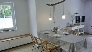 A dining area with a table set for four, surrounded by wicker chairs. A branch with hanging lights is above the table.