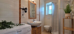 Ein Badezimmer mit weißem Waschbecken, einem an der Wand montierten Fön, Toilette und Duschbereich.