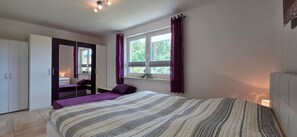 Ein Schlafzimmer mit Bett, Kleiderschrank, Spiegel und einem Fenster mit Vorhängen.
