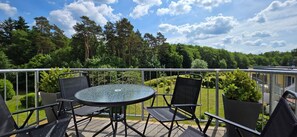 Ein Balkon mit rundem Tisch und vier Stühlen, mit Blick auf einen angelegten Garten und bewaldetes Gelände.