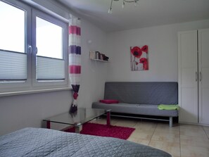 A modern bedroom with a bed, a glass table, a grey sofa, and a red rug.