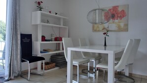 Un coin repas avec une table et des chaises blanches, une bibliothèque blanche et un tableau accroché au mur.