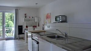 Une cuisine moderne dotée d’un grand îlot central, d’appareils électroménagers en acier inoxydable et d’une porte-fenêtre coulissante donnant sur un balcon.