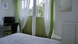 Une chambre à coucher avec un lit, un bureau, une chaise, une télévision et une fenêtre avec des rideaux.