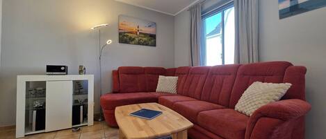 A living room with a red sofa, a wooden coffee table, a white cabinet, and a painting of a lighthouse.