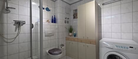 A bathroom with a shower, toilet, and a washing machine.