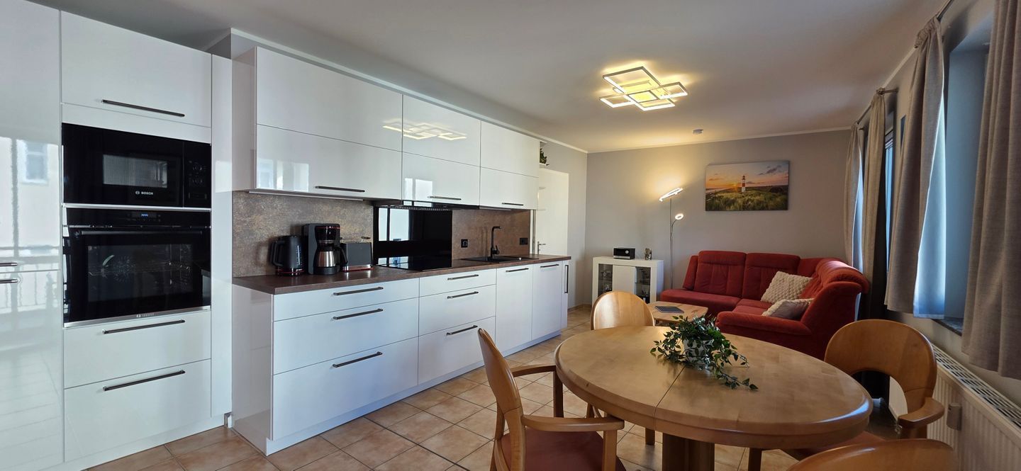 Eine moderne Küche mit weißen Schränken, ein Essbereich mit einem runden Tisch und ein rotes Sofa in einem Wohnraum.