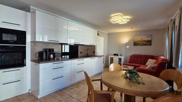 Eine moderne Küche mit weißen Schränken, ein Essbereich mit einem runden Tisch und ein rotes Sofa in einem Wohnraum.