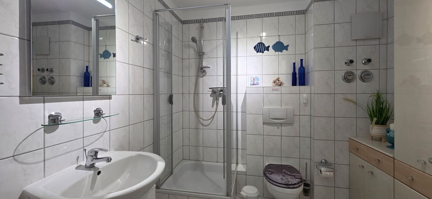 Ein modernes Badezimmer mit einer gläsernen Dusche, einem weißen Waschbecken und einer Toilette.