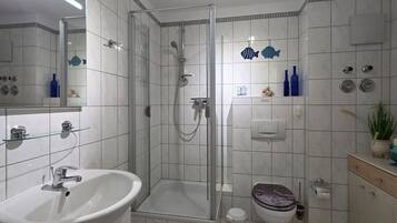 Ein modernes Badezimmer mit einer gläsernen Dusche, einem weißen Waschbecken und einer Toilette.