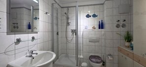 Un baño moderno con ducha envuelta en vidrio, un lavamanos blanco y un inodoro.
