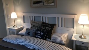 Une chambre à coucher avec une tête de lit blanche, une literie à rayures, deux lampes de chevet et des coussins décoratifs ornés de motifs textuels.