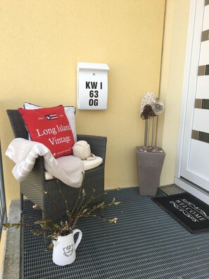 A neatly arranged outdoor seating area with a cushion labeled "Long Island Vintage," a potted plant, and a welcome mat.