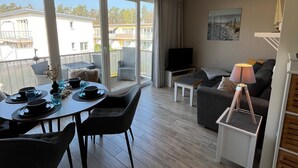 Un appartement moderne comprenant un coin repas, un salon et un balcon offrant une vue sur les immeubles.