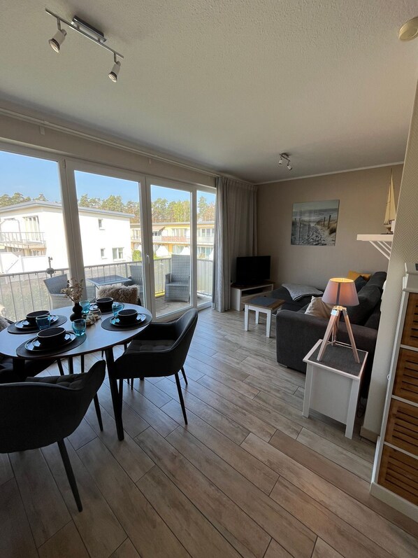A modern apartment with a dining area, a living room, and a balcony with a view of buildings.