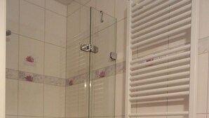 Une douche avec une porte en verre, un mur recouvert de carreaux blancs et un porte-serviettes blanc.